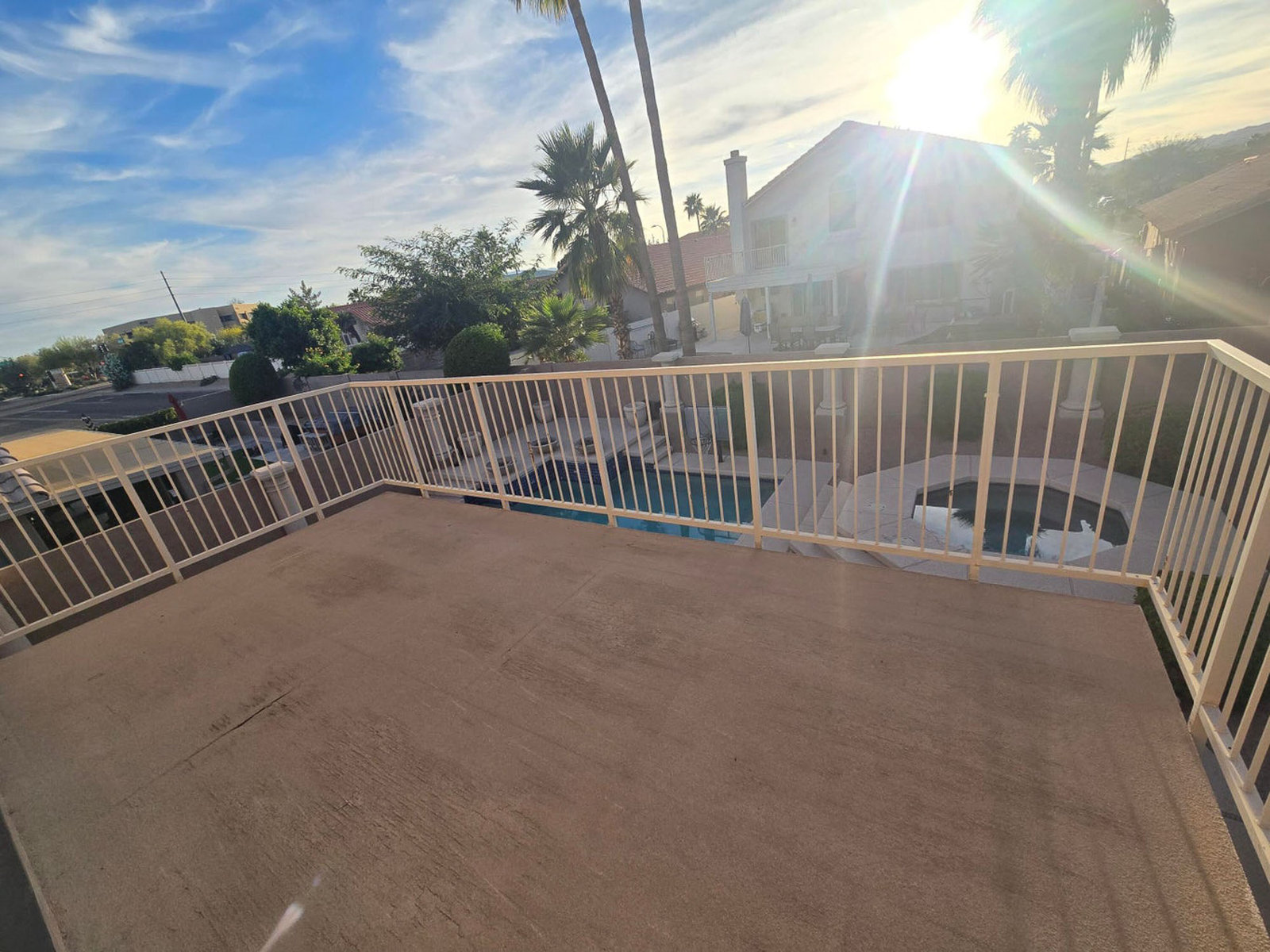 Balcony overlooking a swimming pool and house under bright sun