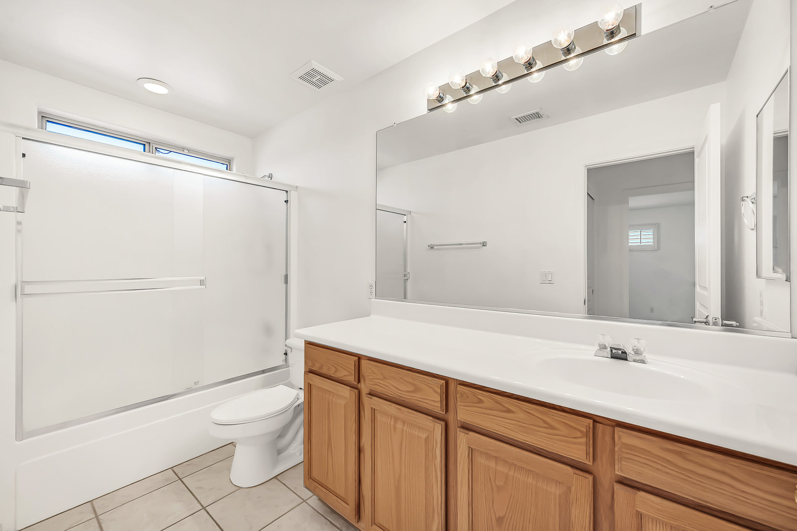 Bathroom with wood vanity, large mirror, and shower