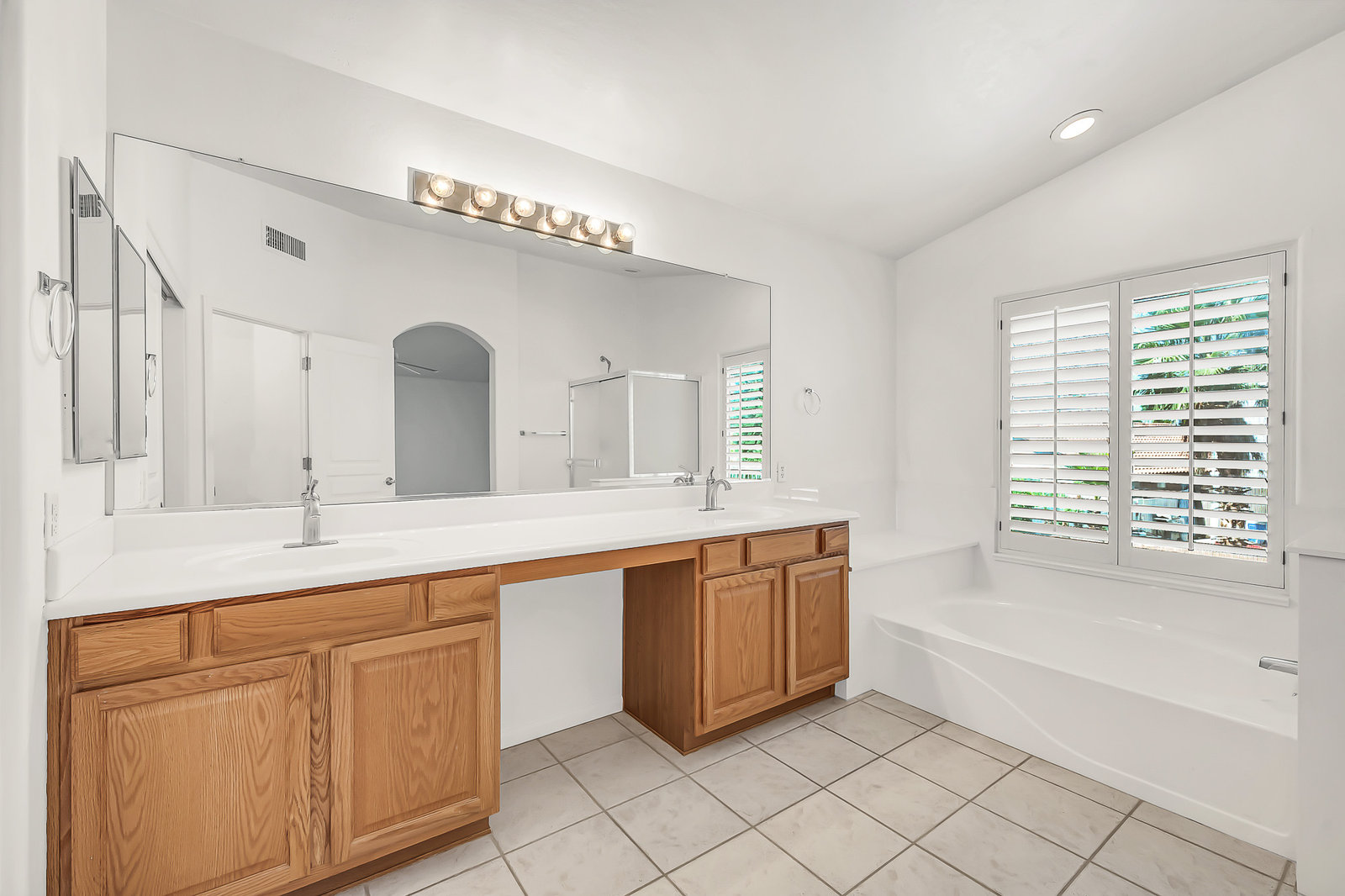 Bright bathroom with double vanity, large mirror, and bathtub.