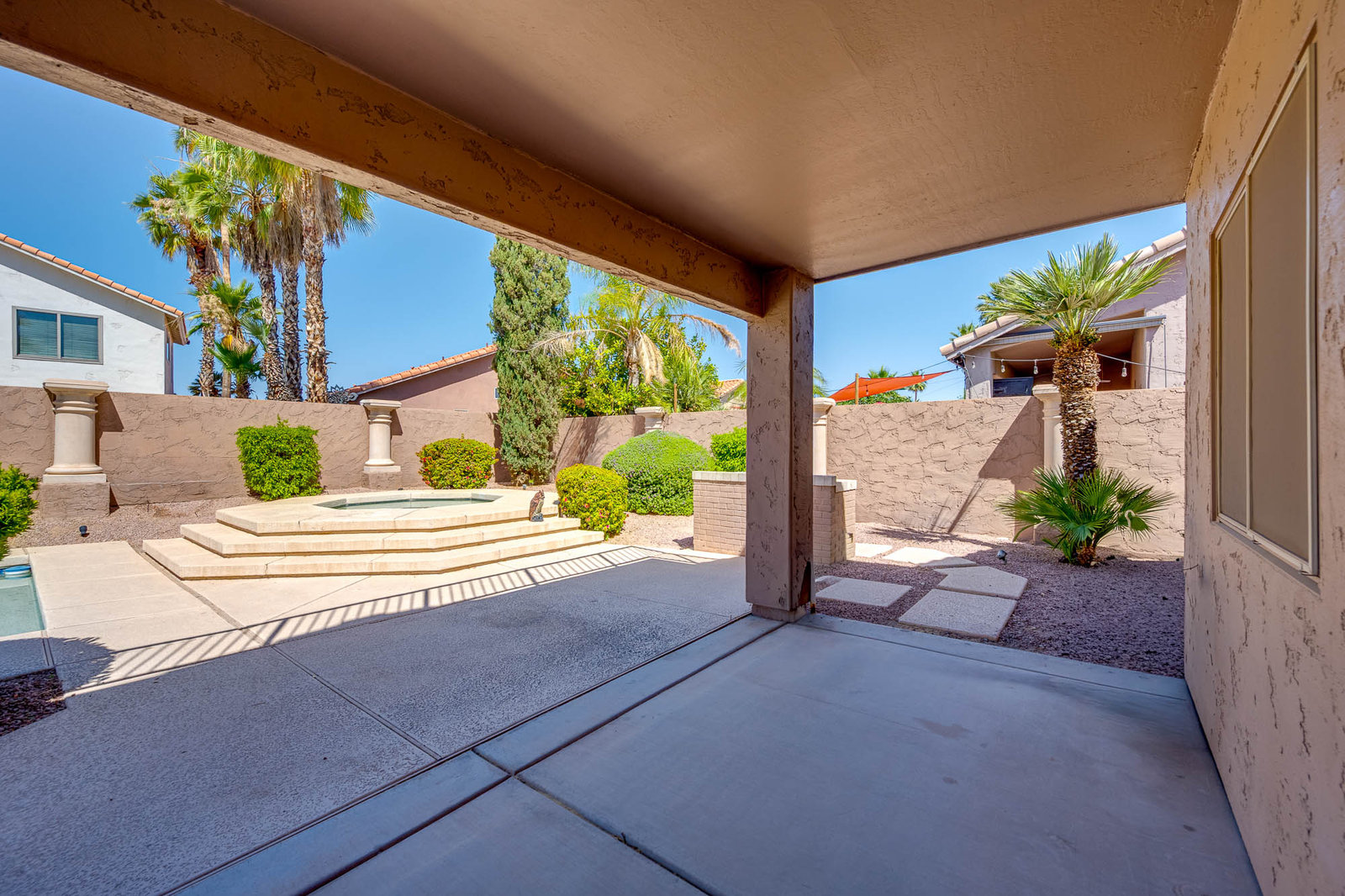 Covered patio with backyard, small pool, and palm trees.
