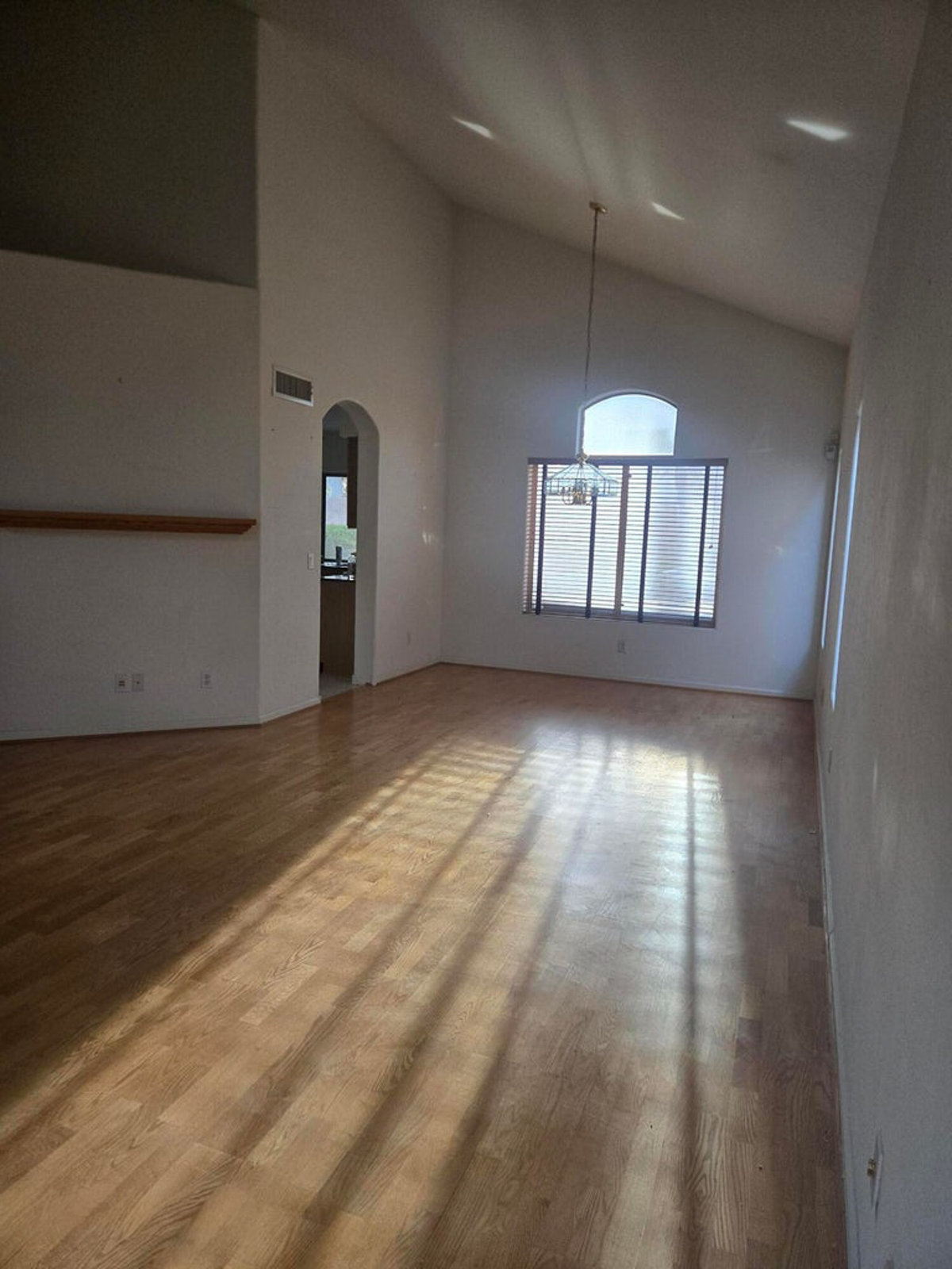 Empty room with wood floor, vaulted ceiling, and sunlit window