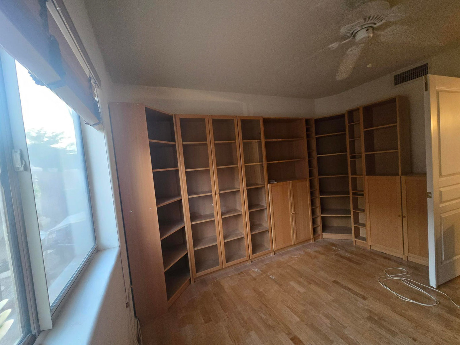 Empty room with wooden bookshelves, large window, wood floor