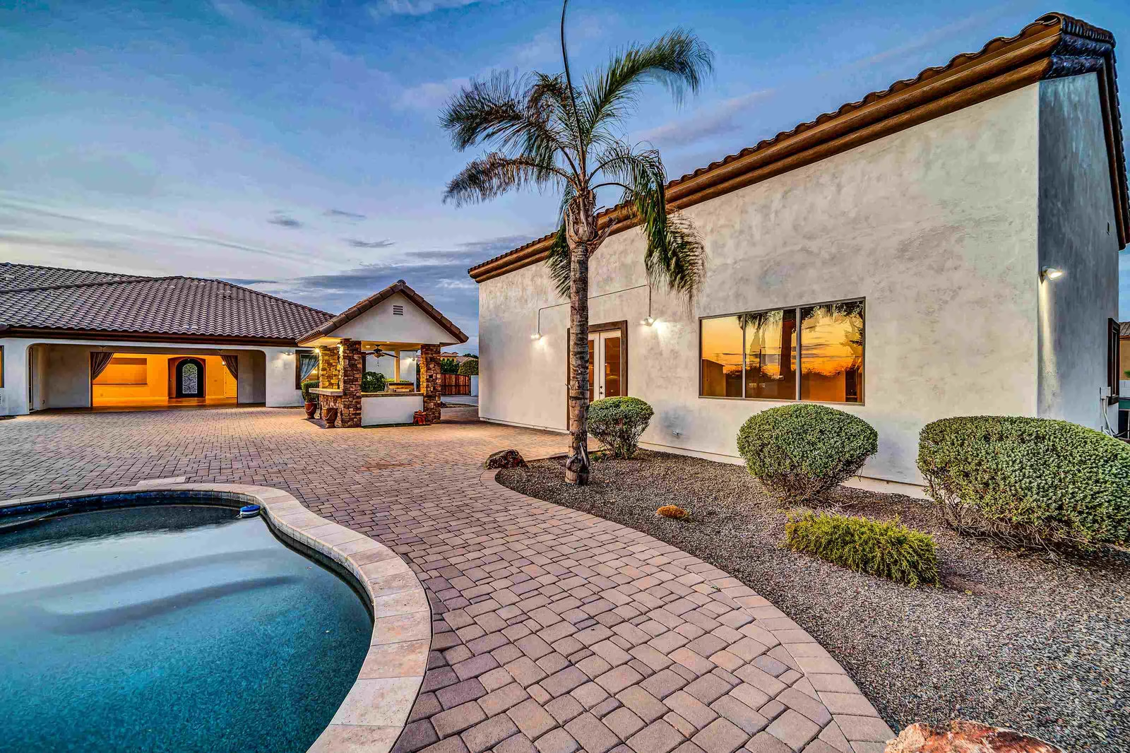 Luxurious house with a pool and paved patio at twilight.