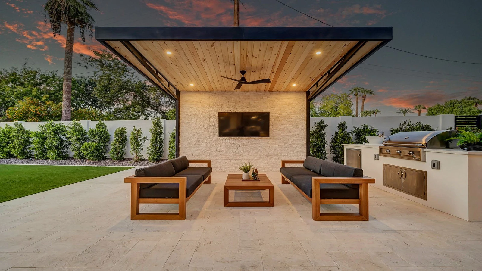 Modern outdoor patio with pergola, seating, TV, and grill at dusk.