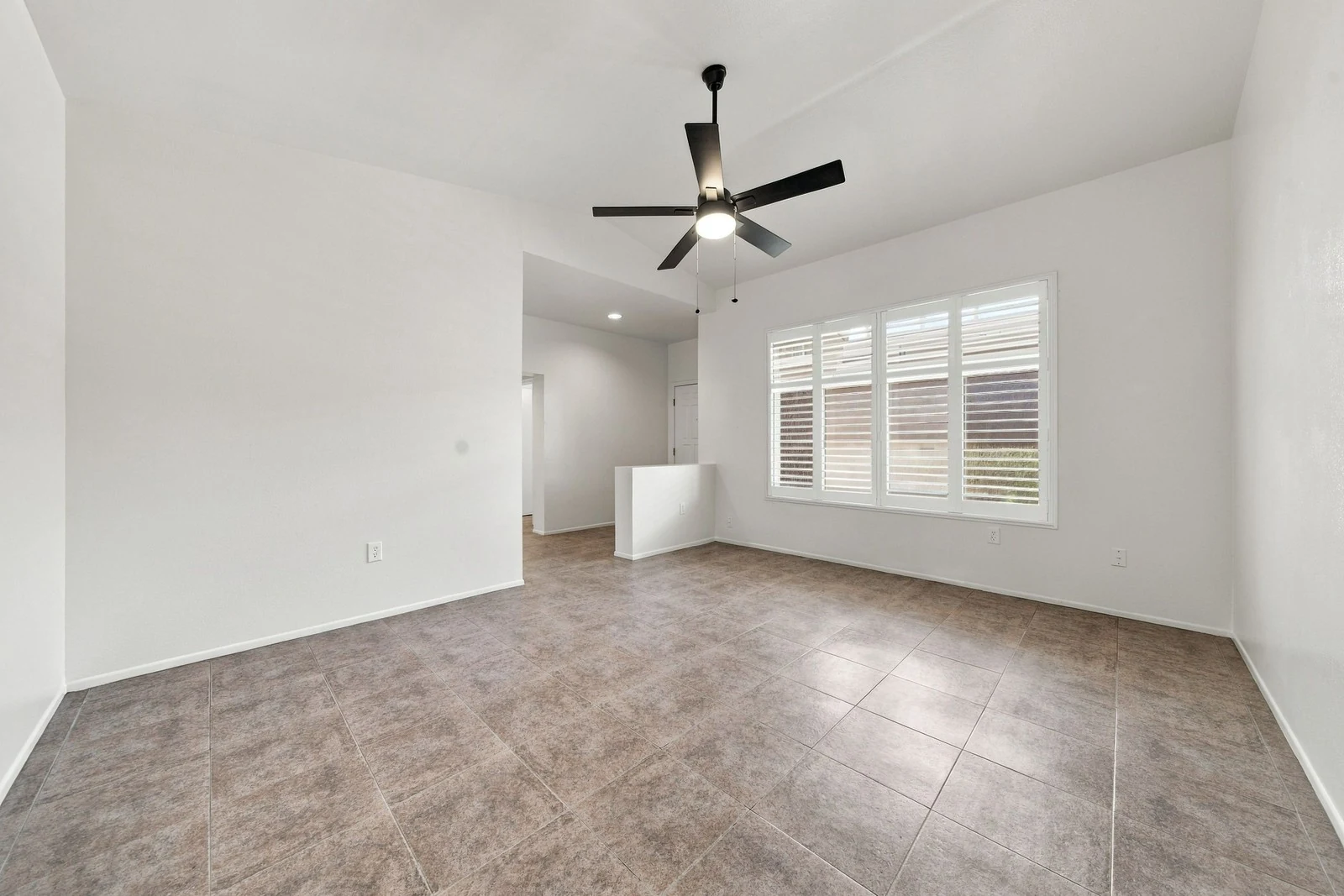 Vacant tiled living room with a ceiling fan and shuttered window